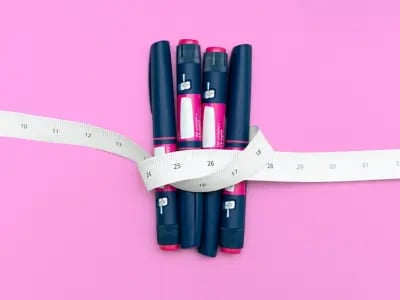 Abnehmspritzen und Maßband auf rosa Hintergrund