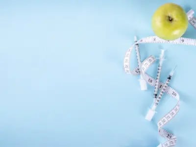 Grüner Apfel, Maßband und Spritzen auf blauem Hintergrund