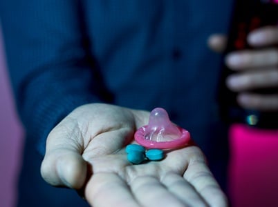 Ein Mann hält eine blaue Pille und ein Kondom in der Hand.