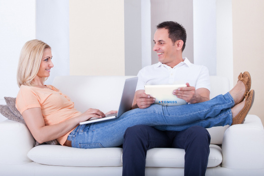 Un homme et une femme sont assis ensemble sur un canapé, concentrés sur un ordinateur portable devant eux.