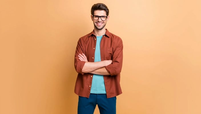 Smiling person with glasses standing with arms crossed against a beige background