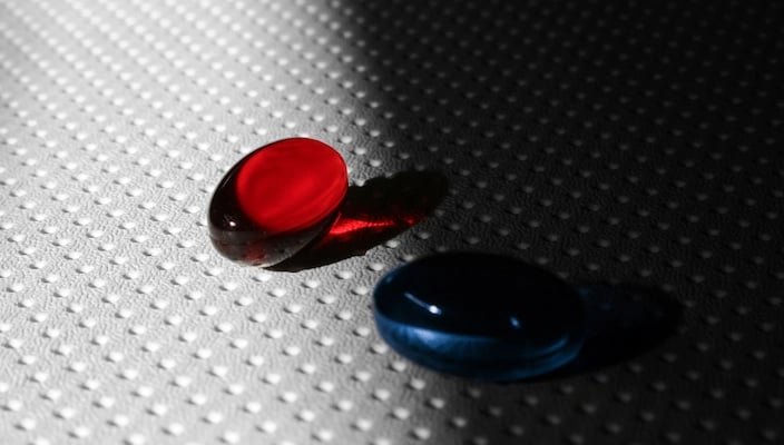 Deux gélules rouge et bleue sur une surface texturée, avec un éclairage contrasté